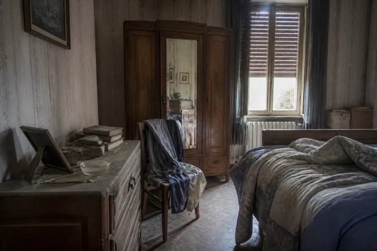 Une chambre restée fermée : volets tirés, poussière épaisse et effets personnels encore en place.